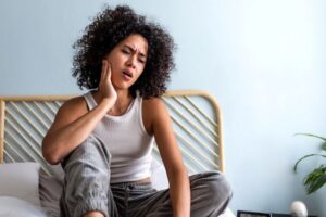 Woman sitting on her bed, suffering from jaw pain 