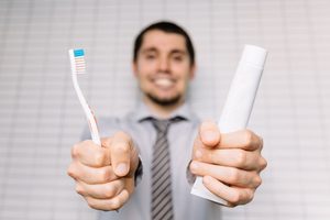 Man in professional outfit holding toothbrush and toothpaste 
